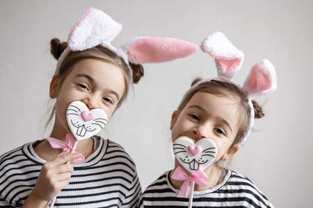 Two funny little sisters are posing with Easter gingerbread in the form of bunny faces.の写真素材