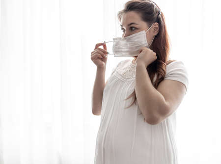The expectant mother in a white T-shirt with a protective mask against the virus on her face.の写真素材
