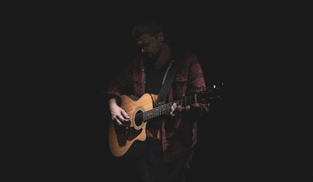 Male guitarist playing acoustic guitar in dark room.