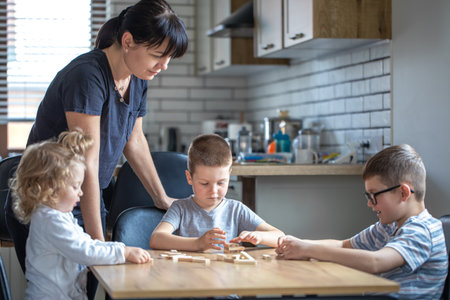 Little children play board game with wooden cubes at home in the kitchen with mom.の写真素材