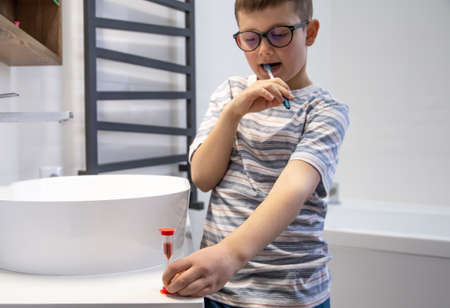 A cute little boy brushing his teeth and timing the hour with an hourglass.の写真素材