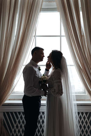 Cute portrait of the bride and groom by the window. Wedding photo session.の写真素材