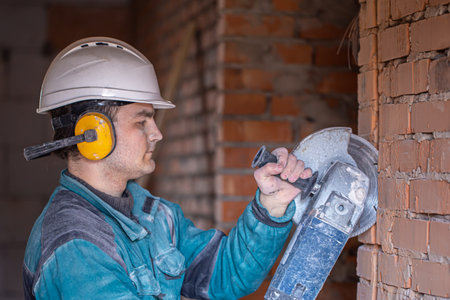 Close-up of a builder in a protective helmet at a work facility works with a cutting tool.