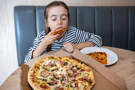 Funny little girl eating pizza in a cardboard box for lunch.の写真素材