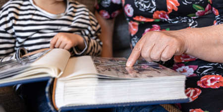 A grandmother with her little granddaughters looks at family photos in photo albums.の写真素材