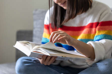 Close-up of an open book in the hands of a girl in a bright colored sweater.の写真素材