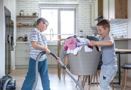 Two funny little brothers help with housework, vacuum and help mom with laundry.の写真素材