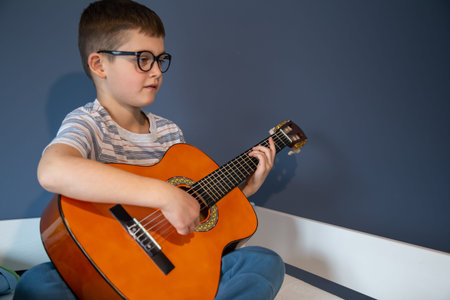Cute boy with glasses learns to play the classical guitar at home.