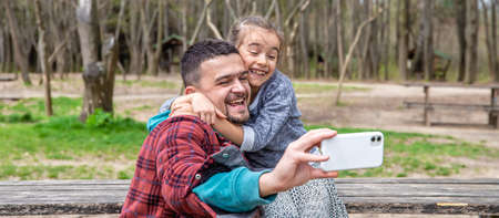A little girl and dad are photographed on the front camera in the park in early spring.の写真素材