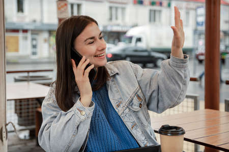 Street portrait of a cheerful young woman on the terrace of a cafe, who is waiting for someone.の写真素材