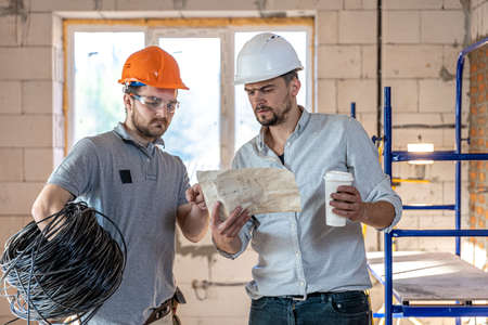 Two builder engineers talking at building site, engineer explaining a drawing to a worker.の写真素材