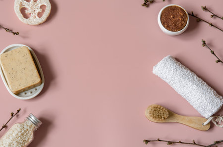 Spa composition with soap, brush, loofah, sea salt and towel among spring tree branches top view.