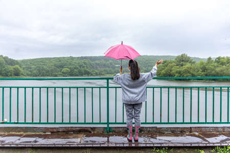 A girl walks under an umbrella in rainy weather on a bridge in the forest.の写真素材