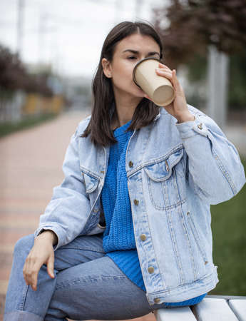 Young woman drinking coffee to go sitting on a bench in the park ..の写真素材