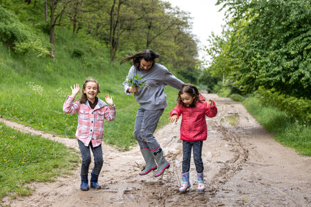 Mom and daughters are walking in the forest after rain in rubber boots in the spring.