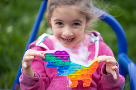 Popular colorful anti-stress toy pop in the shape of a dragon in the hands of a little girl.の写真素材