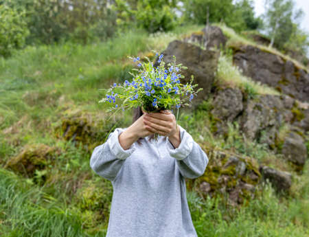 The girl hides her face behind a bouquet of fresh flowers collected in the forest.の写真素材