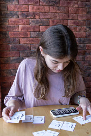 A girl studies musical notes using an application on her phone and educational cards.の写真素材