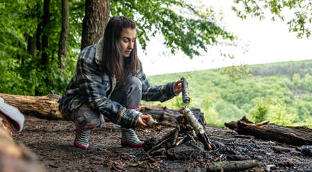 An attractive young woman makes a fire to keep warm in the forest.の写真素材