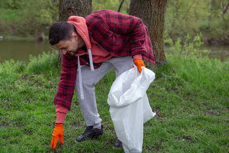 A male volunteer with a garbage bag cleans up the environment in the forest.の写真素材