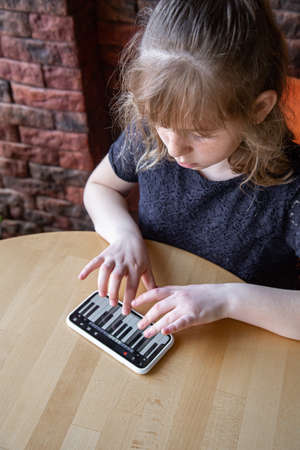 A little girl learns notes in a playful way, with the help of a piano on her phone.の写真素材
