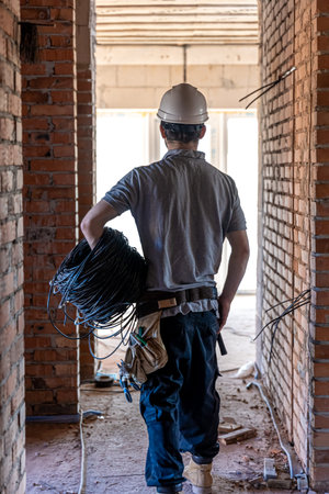 An electrician examines a construction drawing while holding an electrical cable in his hand at a...