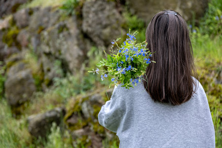 The girl carries a bouquet of flowers collected in the spring forest, view from the back.の写真素材