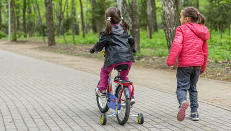 Two little girls ride a bike in the park in spring.の写真素材