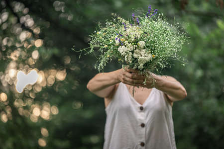 A bouquet of wild flowers in the hands of a girl on a blurred background in the forest.の写真素材