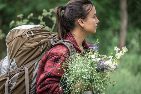 Attractive girl with a large travel backpack and a bouquet of wildflowers.