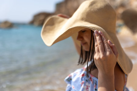 A young woman hides her face from the sun under a large hat on the seashore.