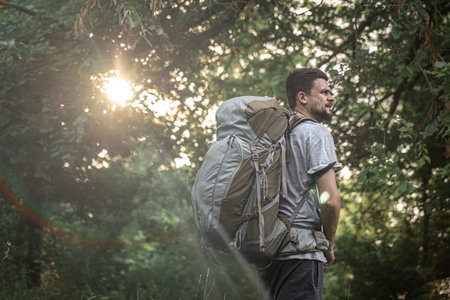 Hiker on a hike with a large backpack on a blurred background of the forest.