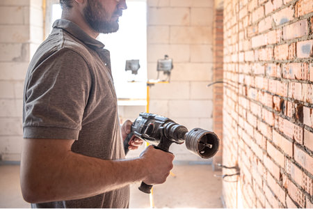 Handyman at a construction site in the process of drilling a wall with a perforator.