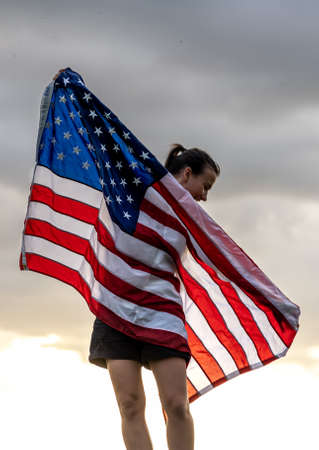 Young woman with United States flag enjoying sunset in nature.の写真素材