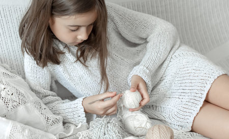 Little girl sitting on the sofa with threads, home leisure concept, crocheting.