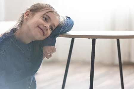 Cute little girl leaning on the table and looking into the distance, back to school concept.の写真素材