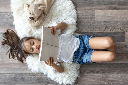 The child reads a book lying on a cozy rug at home with his favorite toy teddy bear.の写真素材