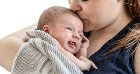 A young mother holds her newborn son in her arms and kisses, on a white background close up.