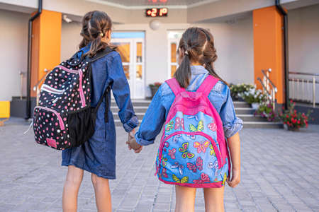 Little girls, primary school students, go to school with backpacks, holding hands.の写真素材