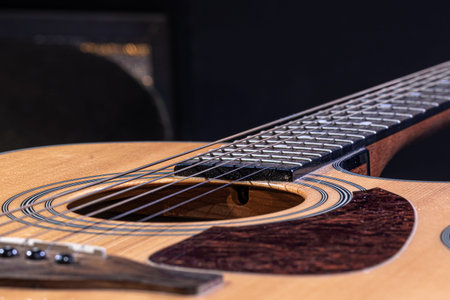 Part of an acoustic guitar, guitar fretboard with strings on a black background.