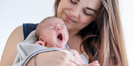 Portrait of a mom with a sleepy newborn son on a white background.