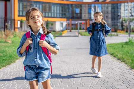 Pupils of primary school. Girls with backpacks near building outdoors. Beginning of lessons. First day of fall.の写真素材