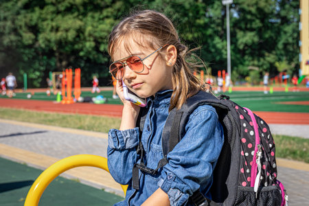 A little girl, an elementary school student in sunglasses phoning, just talking, communication.