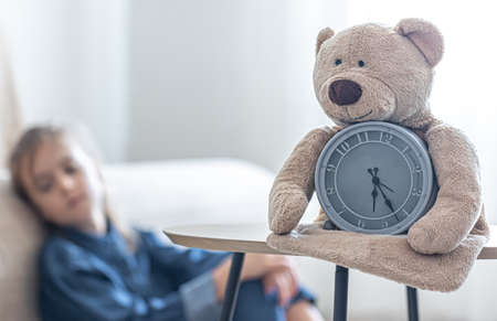 Teddy bear with an alarm clock on a blurred background of a little girl's room.の写真素材