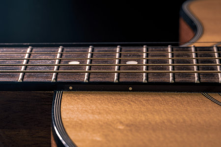 Part of an acoustic guitar, guitar fretboard with strings on a black background.