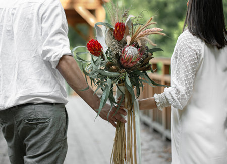 Back view, a couple in love holding a bouquet with exotic protea flowers.の写真素材