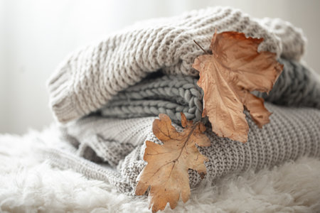 Close-up of a stack of knitted sweaters with autumn leaves on a blurred background.の写真素材