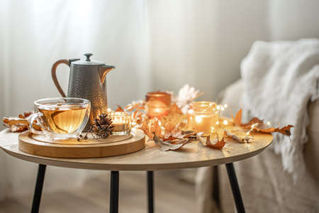 Home autumn composition with tea, dry leaves and burning candles on blurred background, copy space.の写真素材