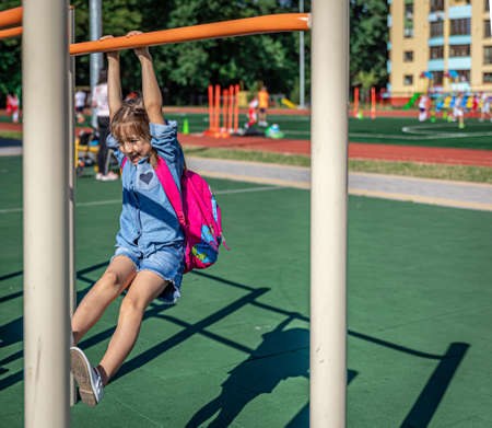 A little girl, an elementary school student, plays on the playground after school, pulls herself up on a horizontal bar.の写真素材