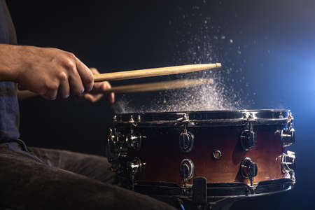 Drummer using drum sticks hitting snare drum with splashing water on black background under studio lighting close up.の写真素材